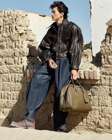 Large Yore Bowling Bag in Moss with white contrast stitching, held by a man in a leather jacket and wide-leg jeans.