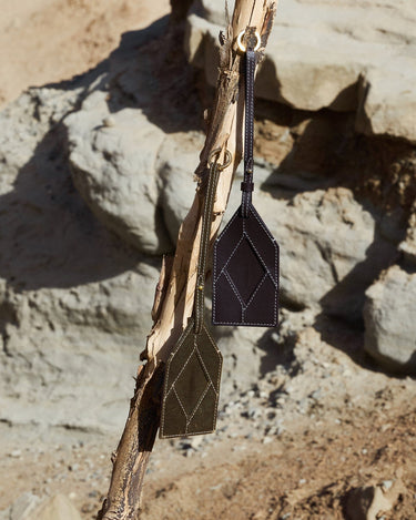 Dark brown and olive green leather bag charms with diamond stitching, hanging from a branch.