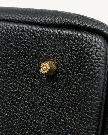 Close-up of a black full-grain leather tote bag showing its pebbled texture and a brass snap with 'Songmont' embossed.