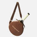 Brown Songmont leather tennis racket cover with adjustable strap, carrying a tennis racket.