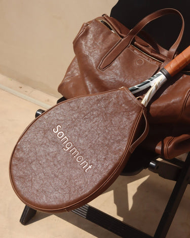 Brown leather tennis racket cover with 'Songmont' embossed, alongside a matching leather bag and tennis racket.