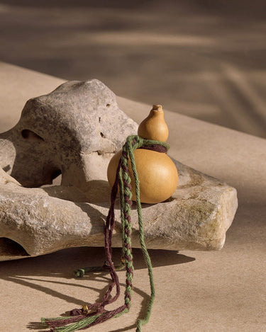 Cypress Lucky Gourd Charm with braided cords and gold accents on a stone.