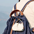 White leather Lucky Pouch Charm with adjustable strap, attached to a denim backpack.