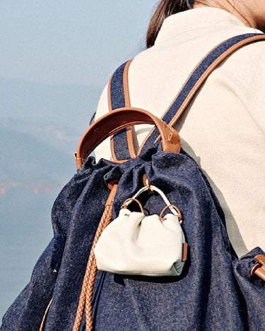 White leather Lucky Pouch Charm with adjustable strap, attached to a denim backpack.