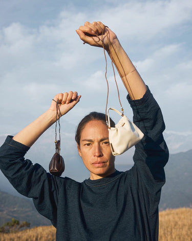 Woman holding a dark brown and an off-white full-grain nappa leather Lucky Pouch Charm with adjustable straps.