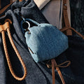 Blue denim lucky pouch charm with leather strap detail, attached to a dark denim bag.