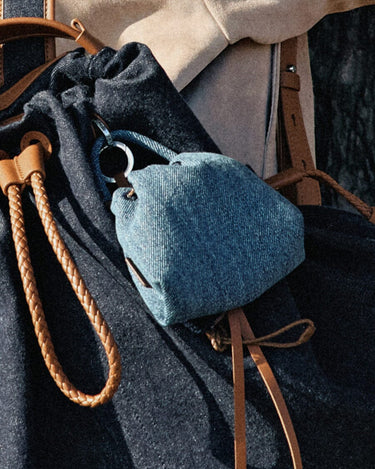Blue denim lucky pouch charm with leather strap detail, attached to a dark denim bag.