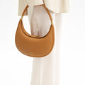 Tan textured leather Luna Bag with gold hardware and embossed Songmont logo, held by a person in cream clothing.