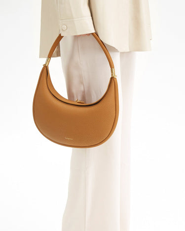 Tan textured leather Luna Bag with gold hardware and embossed Songmont logo, held by a person in cream clothing.