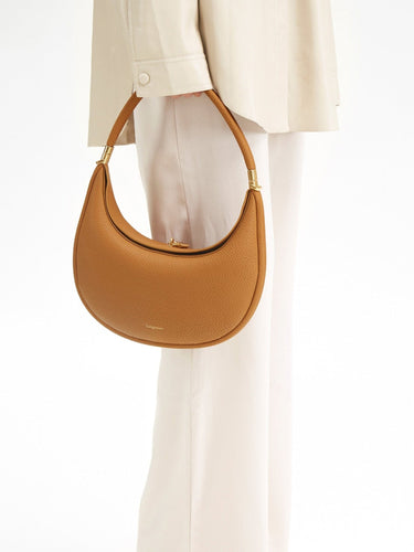 Tan textured leather Luna Bag with gold hardware and embossed Songmont logo, held by a person in cream clothing.