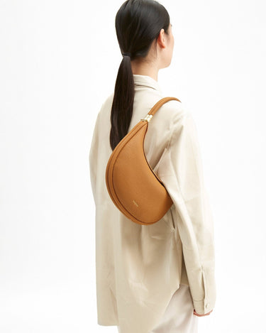 Luna Bag in tan textured leather with gold hardware, worn on the shoulder by a model.