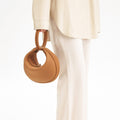 Tan pebbled leather Luna Bag with round handle and gold clasp, worn with a cream outfit.