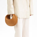 Pebbled tan leather Luna Bag with gold clasp, held by a person in cream outfit