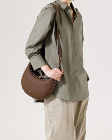 Chocolate Luna Bag crafted from pebbled leather with gold hardware, worn crossbody by a model.
