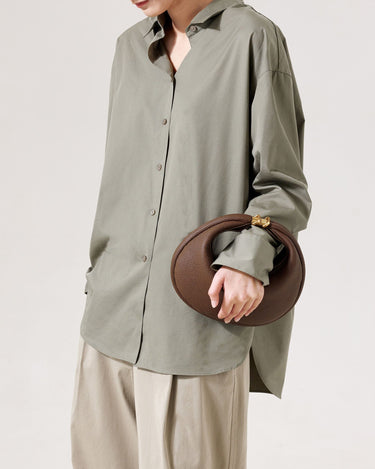 Brown pebbled leather Luna Bag with gold clasp, held by a person in an olive shirt and beige pants.