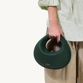 Emerald green Luna Bag with textured leather and circular handle, held by a person wearing a light green blouse.