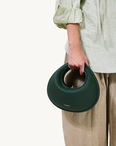 Emerald green Luna Bag with textured leather and circular handle, held by a person wearing a light green blouse.