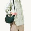 Luna Bag in Emerald green, textured leather with a crescent shape, worn by a model in an oversized light green shirt.
