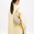 Luna Bag in Ivory pebble-grain leather with gold hardware, worn crossbody by a person in a yellow oversized shirt.