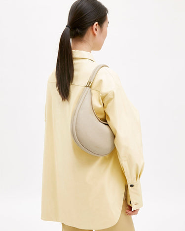 Luna Bag in Ivory pebble-grain leather with gold hardware, worn crossbody by a person in a yellow oversized shirt.