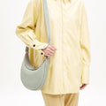 Pale green textured leather Luna Bag with gold clasp, worn by a person in a yellow shirt.