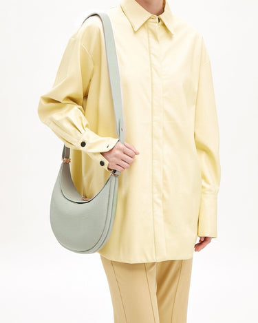 Pale green textured leather Luna Bag with gold clasp, worn by a person in a yellow shirt.