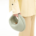 Light green pebbled leather Luna Bag with gold turn-lock closure, held with yellow shirt and beige pants.