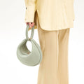 Light green pebbled leather Luna bag with circular handle, paired with yellow shirt and beige pants.