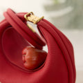 Luna Bag in Lucky Red pebbled leather with brass clasp, featuring a unique curved design.