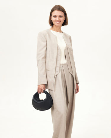 Black Luna Bag with gold clasp held by woman in beige suit. Premium leather handbag.