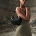 Luna Bag in Onyx black full-grain leather with silver-tone hardware, worn by a model in an olive-green dress.
