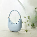 Light blue Luna Bag with pebble-grain leather texture, silver clasp, and curved handle on textured surface.