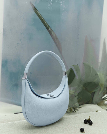 Sky blue Luna Bag, full-grain leather, silver hardware, curved strap, magnetic closure. Elegant and versatile.