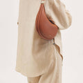 Eco Caramel Luna Bag in vegan leather, crescent shape with gold buckle detail.