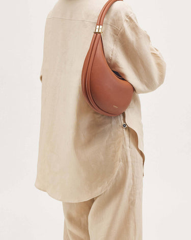 Eco Caramel Luna Bag in vegan leather, crescent shape with gold buckle detail.