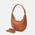 The Luna Bag in Eco Caramel vegan leather features a crescent shape, gold hardware clasp, and a detachable strap.