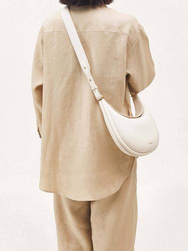 Luna Bag in Eco Cloud vegan leather worn crossbody by a person in a beige linen outfit.