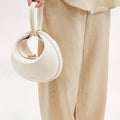 White vegan leather Luna Bag with gold clasp, held by hand. Made from recycled materials.