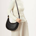 Luna Bag in Eco Onyx vegan leather with gold clasp and dark strap, worn by a model.