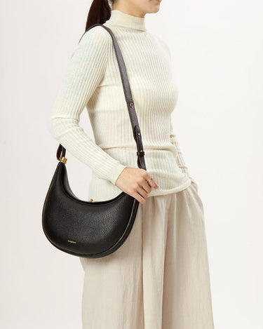Luna Bag in Eco Onyx vegan leather with gold clasp and dark strap, worn by a model.