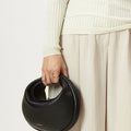 Black vegan leather Luna Bag with gold "Songmont" logo, crescent shape, on a person's hand.