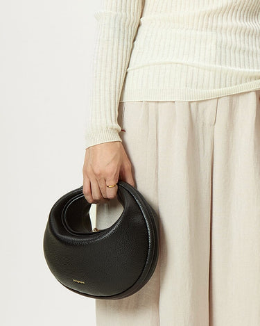 Black vegan leather Luna Bag with gold "Songmont" logo, crescent shape, on a person's hand.