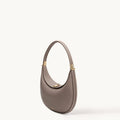Taupe pebbled leather Luna Bag with a curved silhouette and gold hardware.