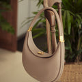 Taupe textured leather Luna Bag with gold hardware, hanging on a wooden chair.