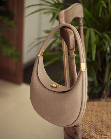 Taupe textured leather Luna Bag with gold hardware, hanging on a wooden chair.