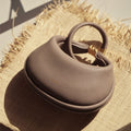 Taupe pebbled leather Luna Bag with gold hardware and circular handle on jute placemat