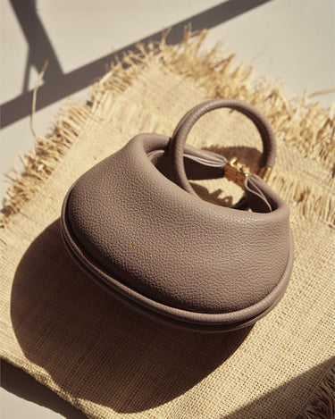 Taupe pebbled leather Luna Bag with gold hardware and circular handle on jute placemat