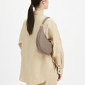 Taupe pebbled leather Luna Bag worn on the shoulder of a woman in a beige linen shirt.