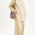 Woman wearing beige linen shirt and wide-leg pants, accessorized with a textured taupe Luna Bag.