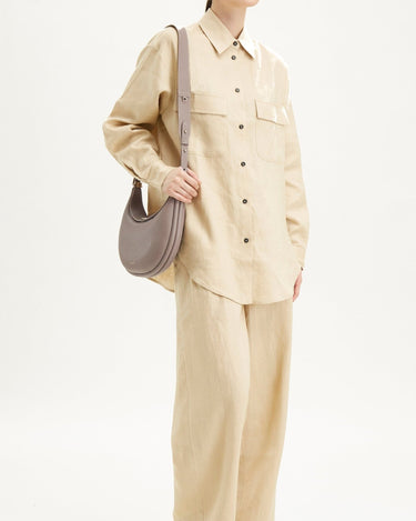 Woman wearing beige linen shirt and wide-leg pants, accessorized with a textured taupe Luna Bag.